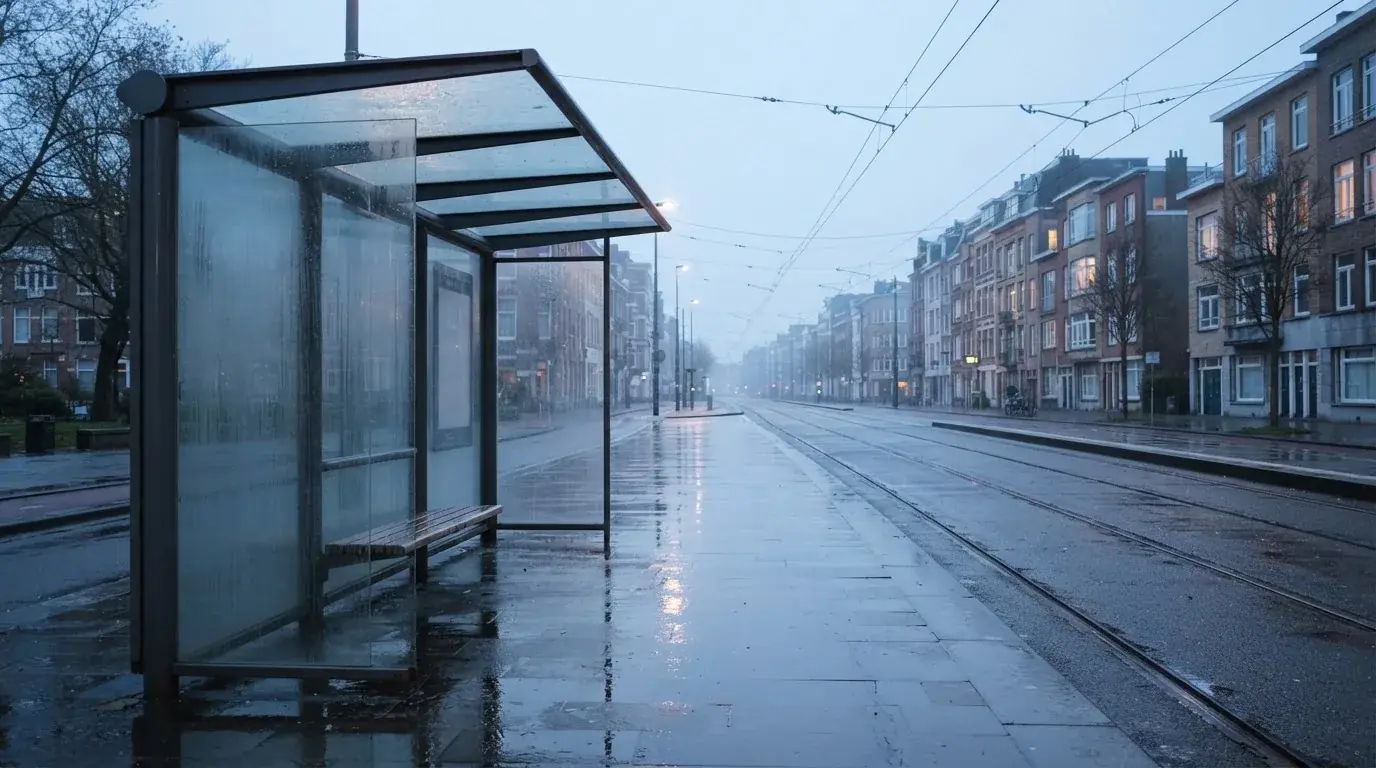Pusta wiata przystanku tramwajowego na miejskiej ulicy o świcie, pusta ławka i mokry chodnik.