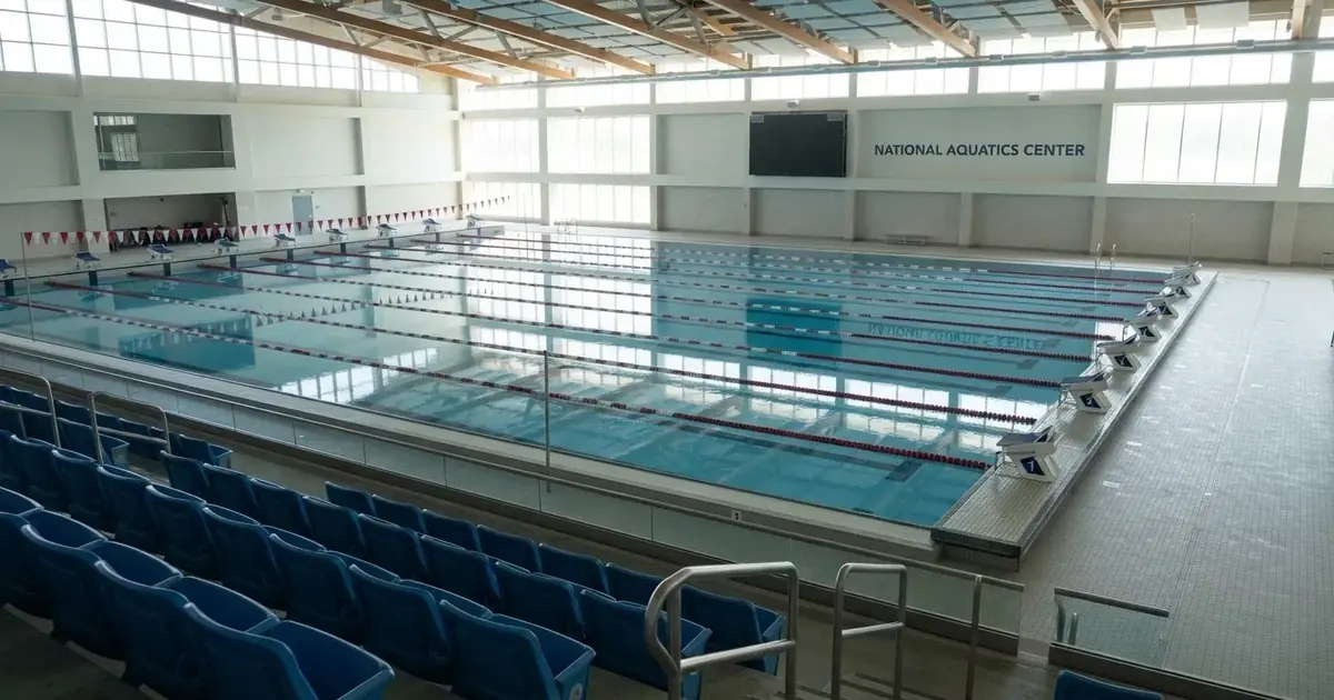 Pusty basen olimpijski z równymi torami i spokojną taflą wody, widok z trybun w jasnym świetle.